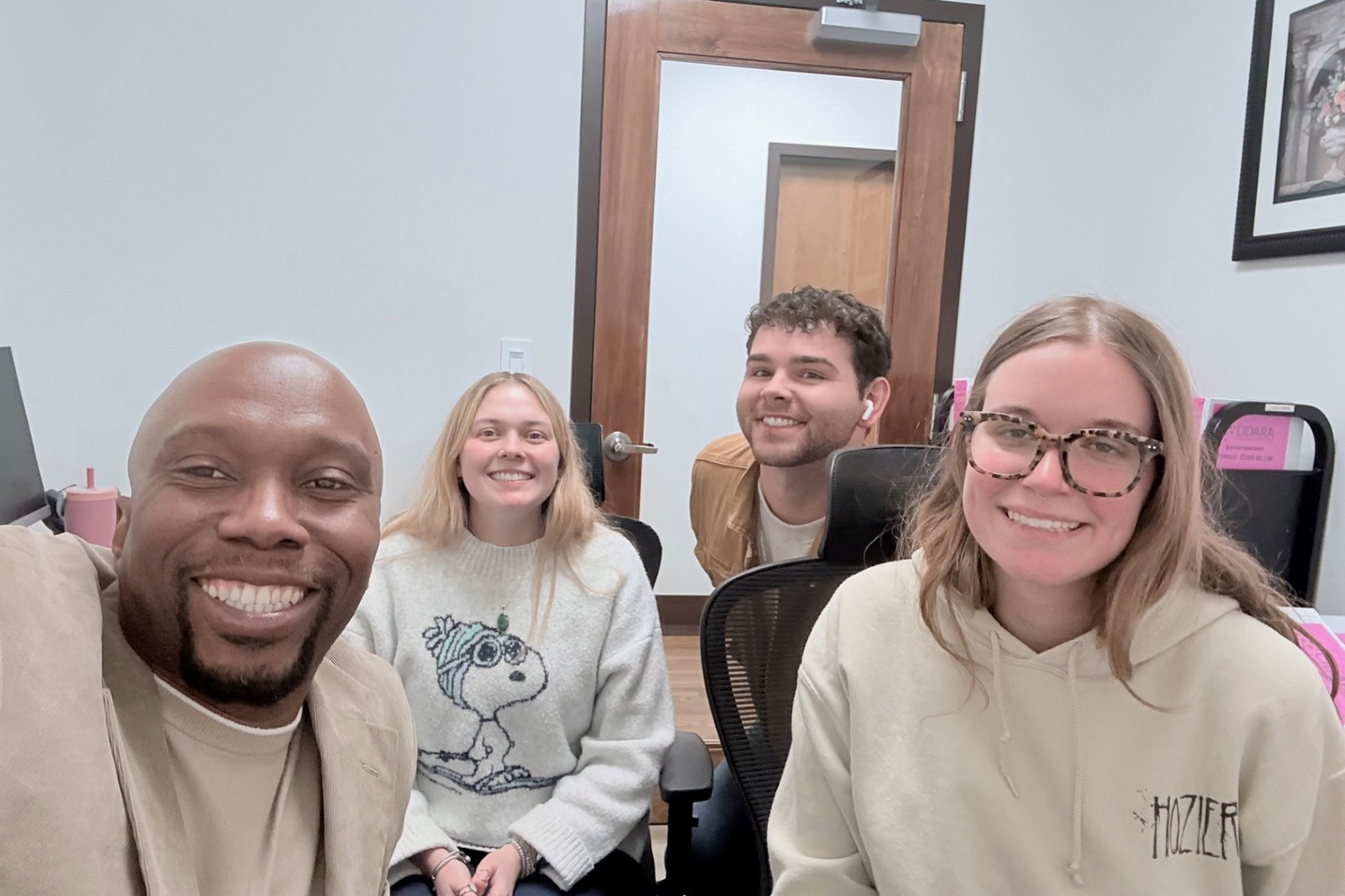 Four professionals  working in the clinical research industry are smiling into the camera. They are sitting down in an office setting wearing business casual.