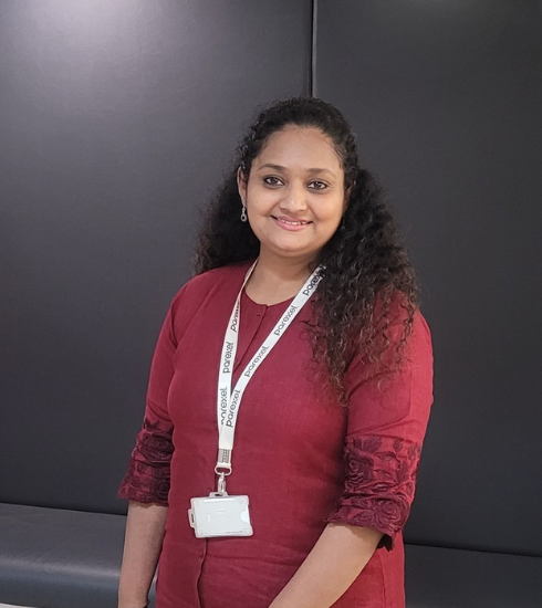 An Indian women wearing a maroon kurta and a lanyard, standing against a dark background.