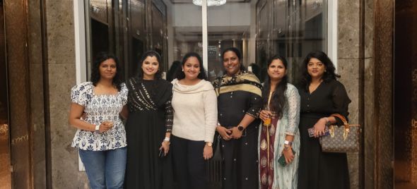 Group of six people standing indoors in front of a glass door, wearing a mix of traditional and modern outfits.