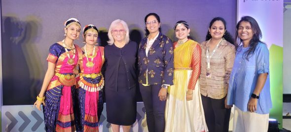 Group of seven people on a stage, two in traditional dance costumes and others in formal and semi-formal attire.