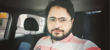 Shadaab, an indian male, with short dark hair, glasses and a dark beard, wearing a white and pink collared shirt.