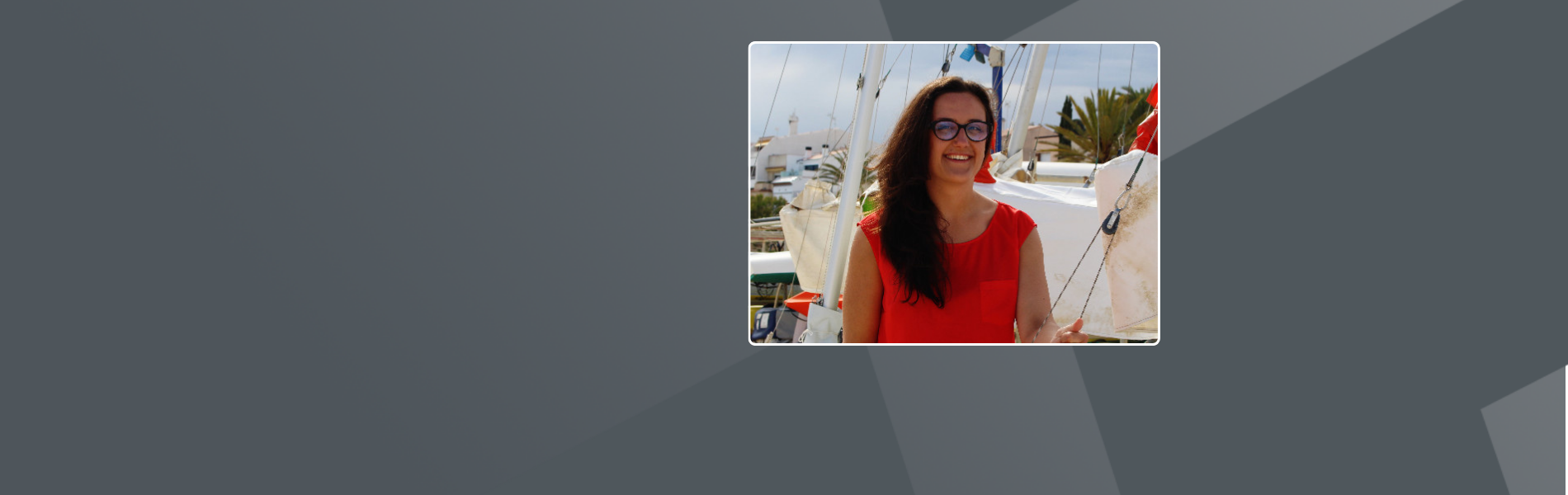 Simona, wearing a red shirt with long brown hair and glasses, standing on a sailboat