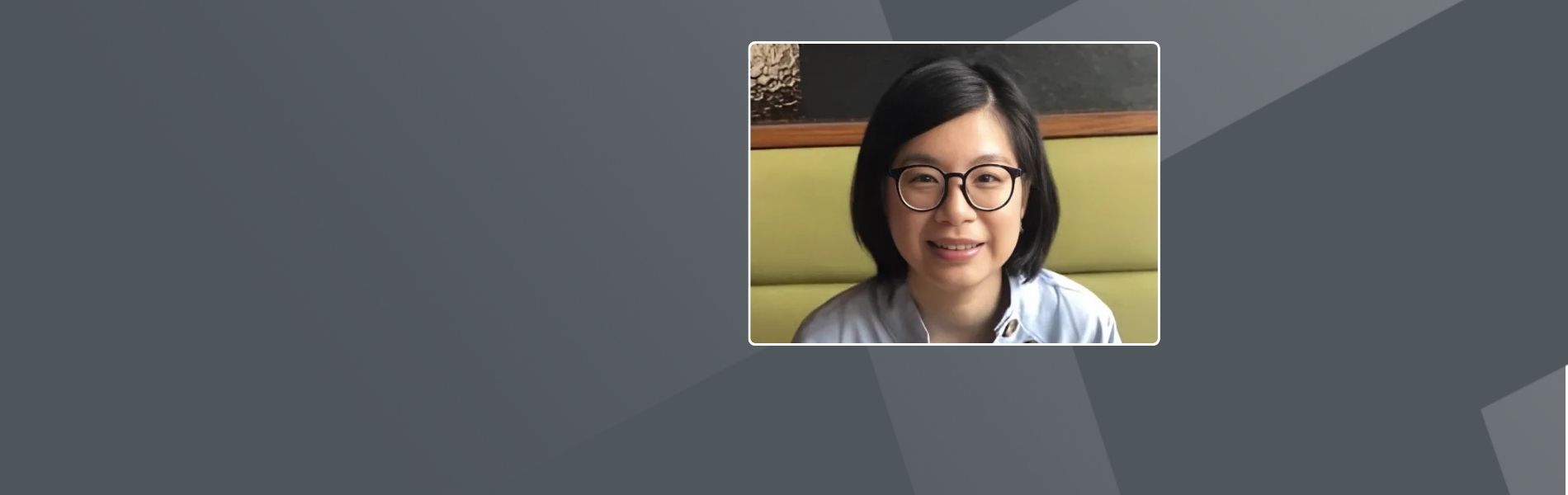 Tina, a Taiwanese woman, with short dark hair wearing round glasses and a light-colored top with decorative buttons, sitting against a green upholstered booth.
