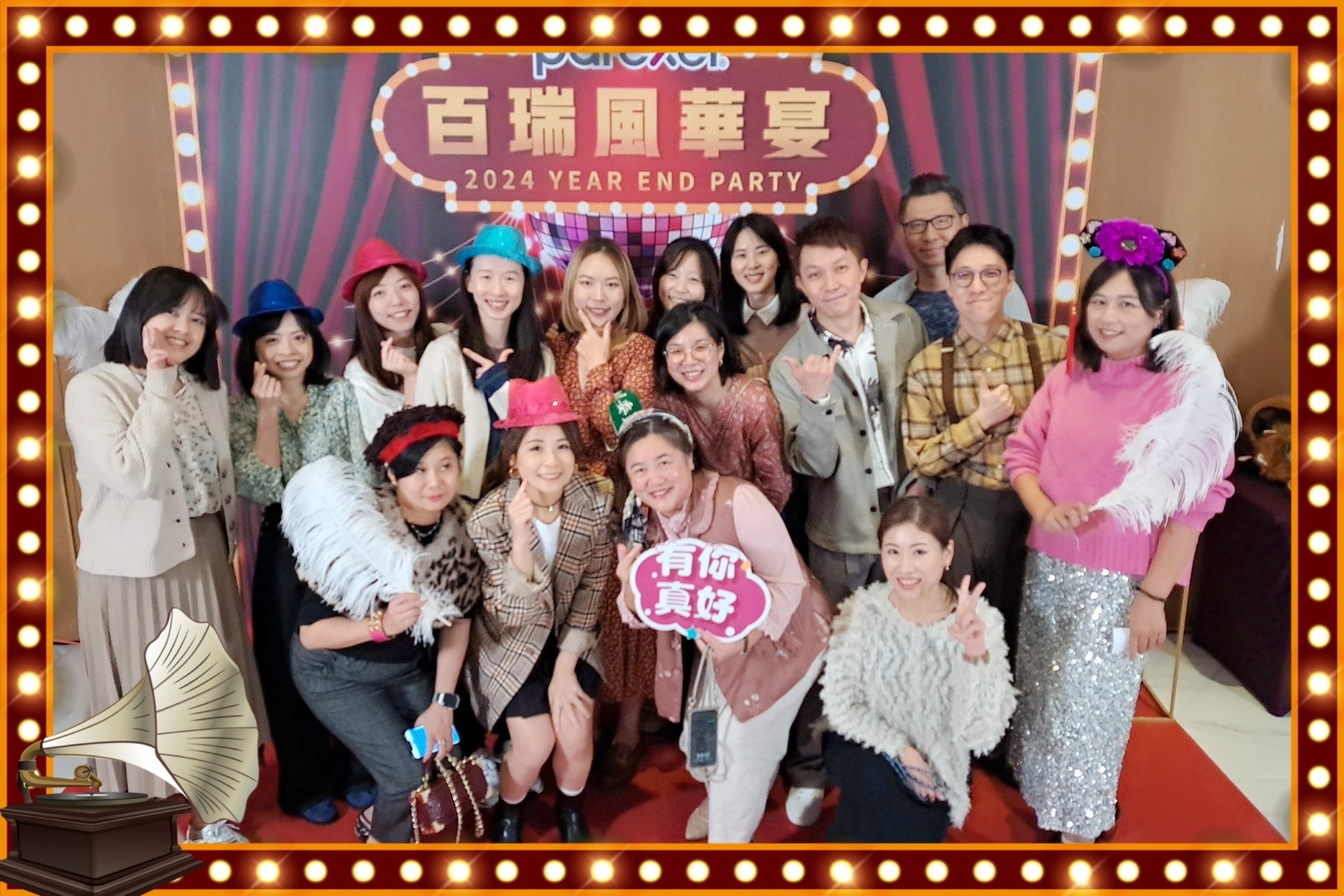 Parexel Taipei team picture. The team is gathered in a colourful space with large cardboard background for event. People are arranged in two rows, wearing casual attire in various colors, smiling at the camera.