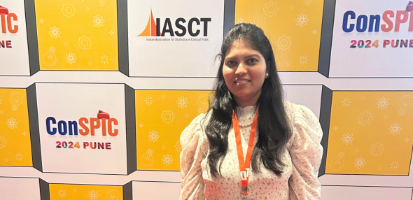 A woman standing in front of a conference backdrop featuring the logos “ConSPIC 2024 Pune” and “IASCT.” She is smiling, wearing a light-colored blouse and an orange lanyard.