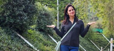 Ruchika has long dark hair, dark eys, and is smiling to the camera, she has a black top on and a blue straped bag across her torso