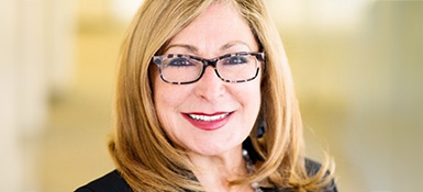 Aida Sabo, a Mexican American female working as Senior VP of Diversity, Equity & Inclusion (USA), with short blonde hair, brown glasses and business attire. She smiles while looking directly into the camera