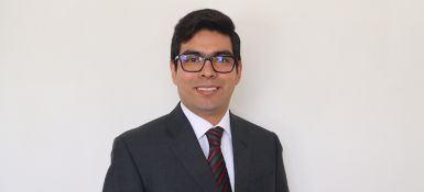 Oscar, brown hair and wearing a black suit and glasses, smiling