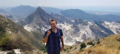 Yuri standing on top of a mountain side with more mountains in the background