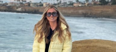 Leah Hasson, blonde long curly hair, wearing a white jacket standing on a beach