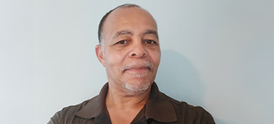 Mark, short hair and beard, wears a brown polo shirt, smiling at the camera.