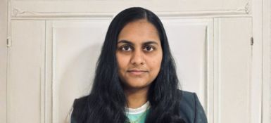 Sravani Manukonda, smiling at the camera wearing a black jacket and light blue shirt