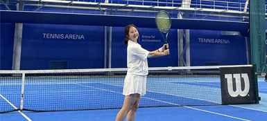 Yena, a Korean Woman, in a blue tennis hall, she is posing with her tennis racquet.