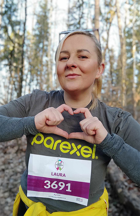 Laura at the Rare Disease Run 2024, wearing a Parexel t-shirt and shaping a heart with her hands.