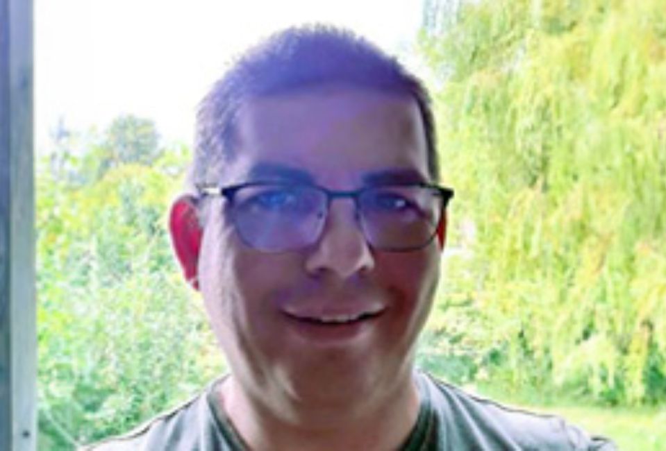 Alan, smiling, wearing a light gray shirt with brown hair and glasses