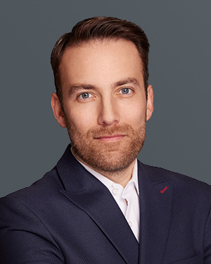 Andreas, a white European man, short dark blond hair, wearing a dark jacket and a white shirt.