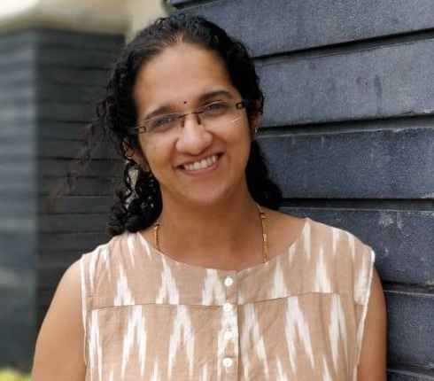 Female Indian with long dark hear, wearing glasses and a patterned top.