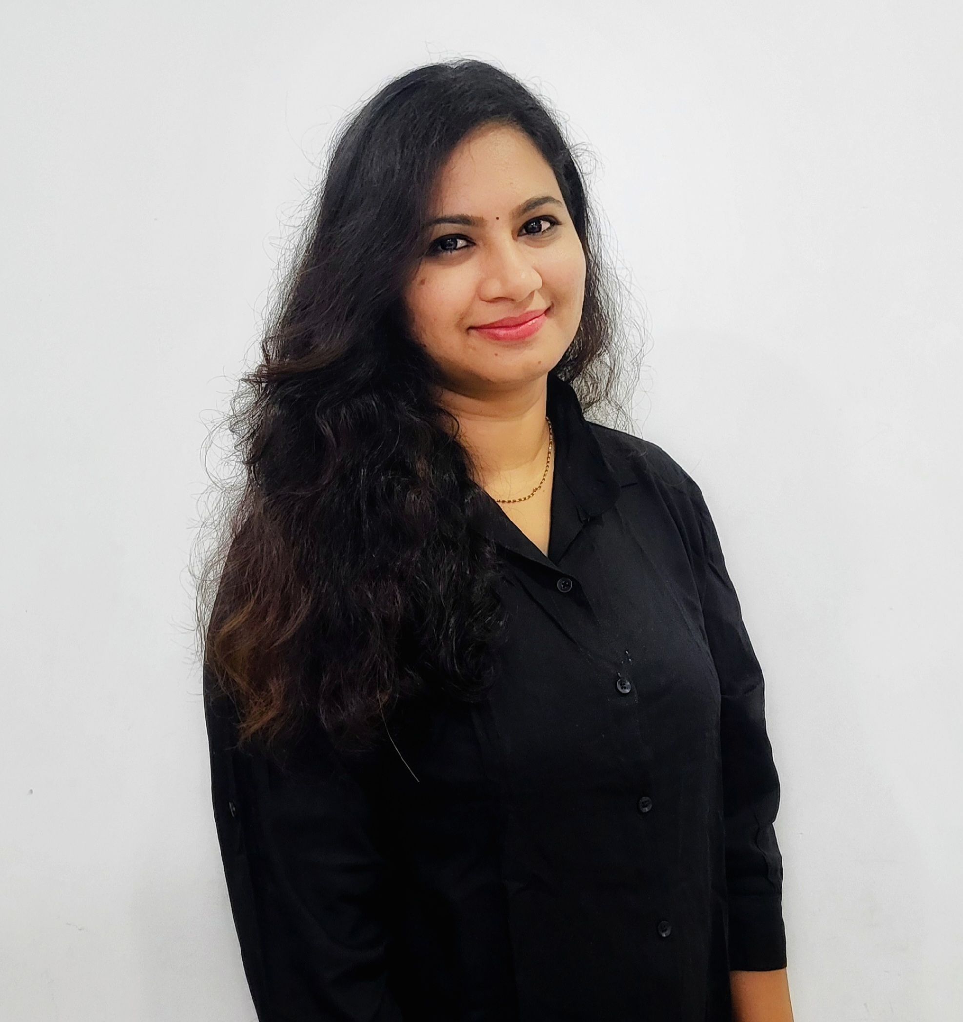 Bindu, long black hair wearing a navy shirt and staring into the camera smiling. white background and tan skin