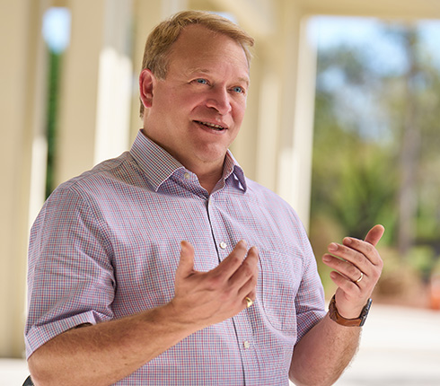 David, a white male Scott with blonde hair, pink shirt outside under cover with blurred background of trees.