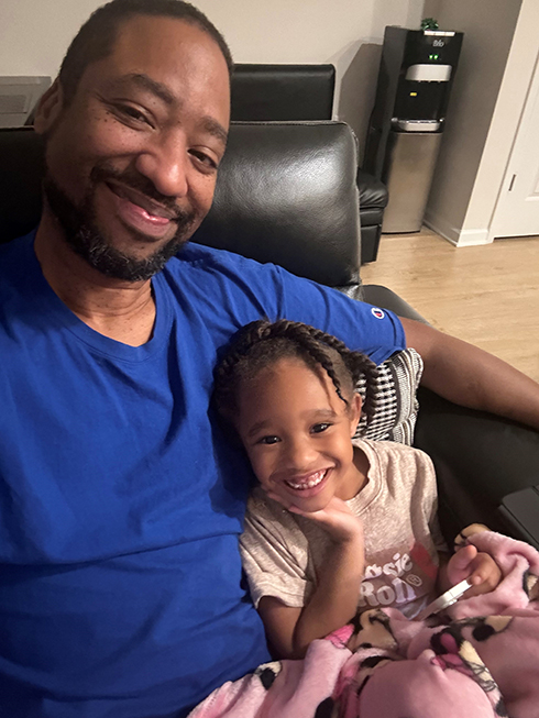 Moe sitting in a chair with his granddaughter in his arm.