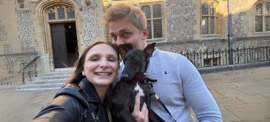 Katherine, smiling at the camera, standing with her husband and dog