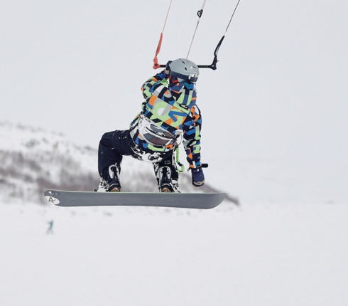 Kirill snowkiting, wearing a colorful abstract jacket, white helmet, and black pants