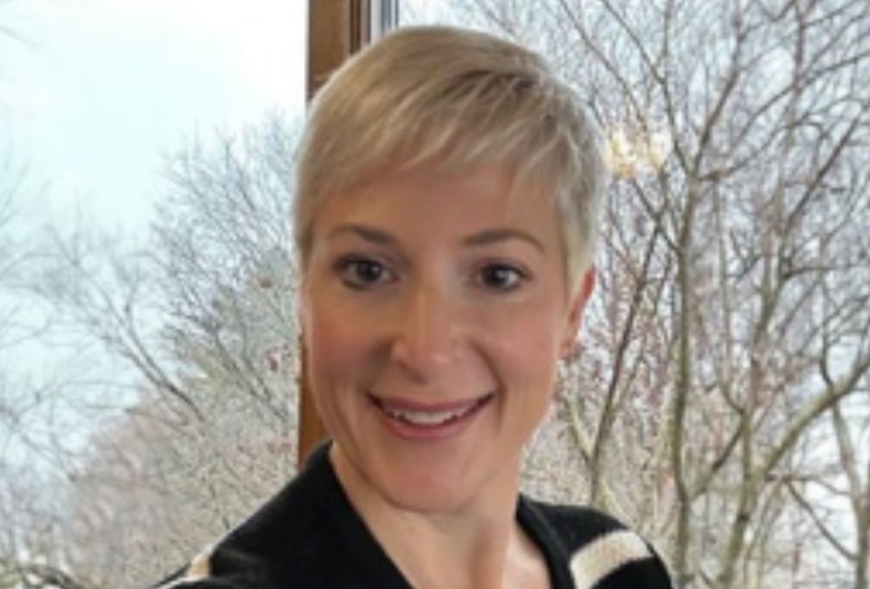 Kris wearing a black sweater with blonde hair, smiling
