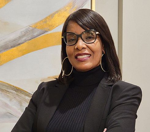 LaTasha, a black American woman, wearing shoulder long straight hair, thin hoops, big black glasses and a black jacket.