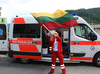 Laura in front of an ambulance, wearing her ambulance work outfit and she is waving the Lithuanian flag, her home country.