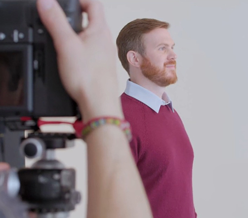 Matt, at the photo shooting for the campaign. Camera in the front with a hand, and Matt in the background looking to the side.