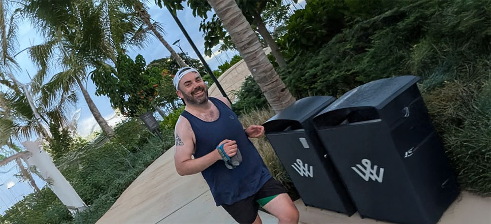 Patrick Grimes, an Associate Director of Statistical Programming at Parexel, is outdoors running at a park. He is wearing running gear with a black cap and smiles