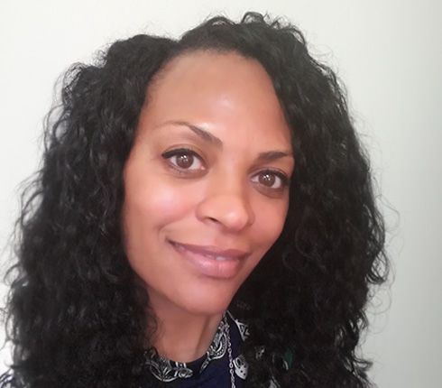 Ramona, a black American woman, wearing long dark curly hair and a pattern shirt.