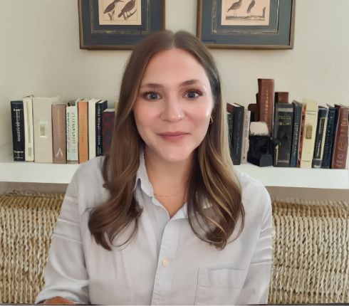 Renee Farrow is smiling at the camera, with long brown curled hair and wearing a light blue button up shirt.