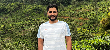 Ruthvik, a Statistical Programmer at Parexel, male, tanned skin smiling at the camera and outside in nature green trees and bush