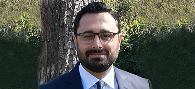 Sinan, VP Technical of Regulatory Strategy, with short dark hair and beard, wearing black glasses and a professional attire. Smiling into the camera.