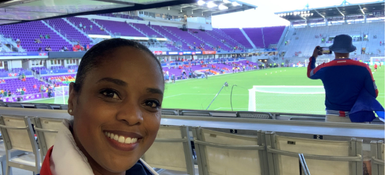 Yoela, a Black American female, smiling towards camera with her hair tied back.