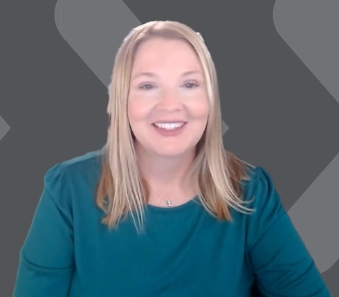 Screenshot from the video of Kelly. She is an American woman with long blonde hair wearing a teal top. She has a friendly expression and is positioned against a gray background with angular shapes.