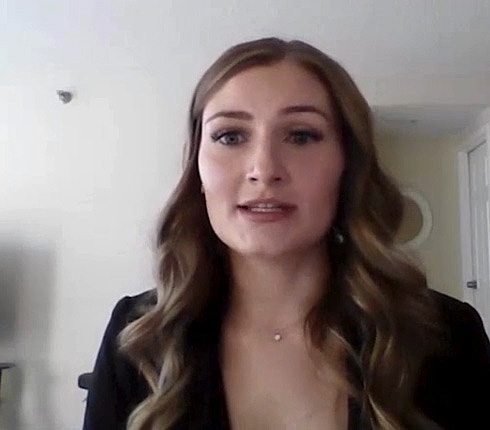 Kylie, a white American woman with long wavy blonde hair. She wears a black blazer and delicate necklace. The background shows a plain white wall in what appears to be an indoor setting.