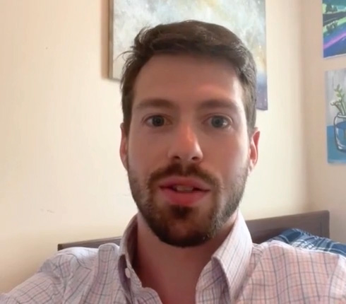 Rick, a white man with short dark hair and a beard, wearing a light-colored button-down shirt. Behind him are walls with framed artwork.