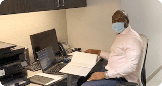 Male employee with medical mask on sitting at desk with laptop open