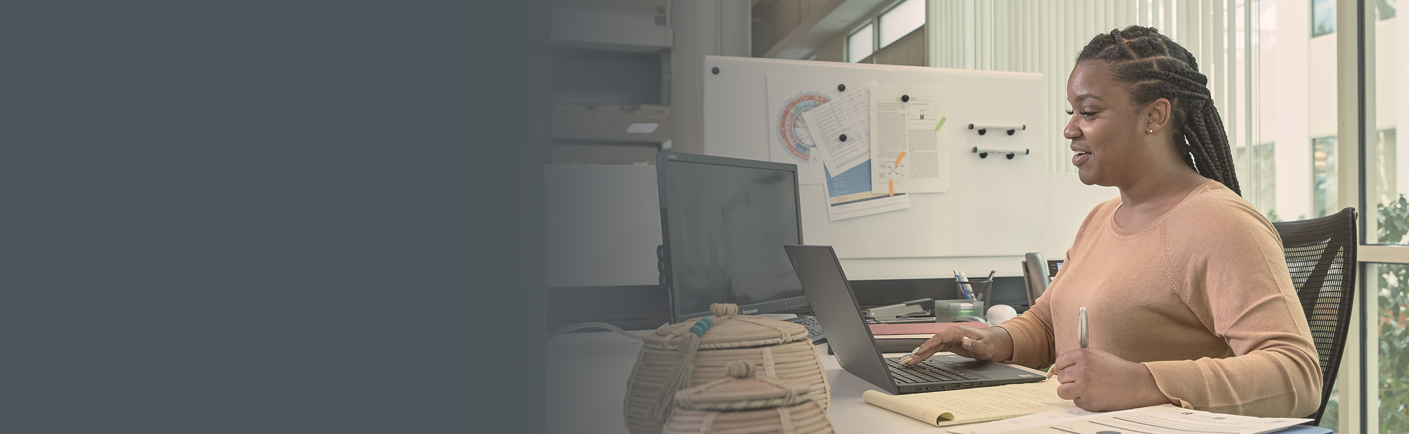 Woman seating at a cubicle in an office, holding a coffee mug.