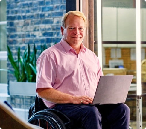 David, a male white Scot, short blond hair, wears a pink shirt and sits in a wheelchair.