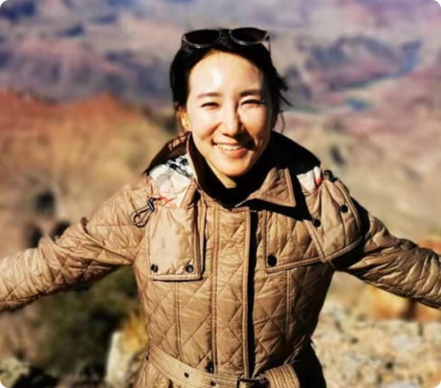 Nayoung, a female South-Korean and Vice President, Enterprise Account Leader at Parexel, she is standing in front of a canyon, arms spread, smiling at the camera.