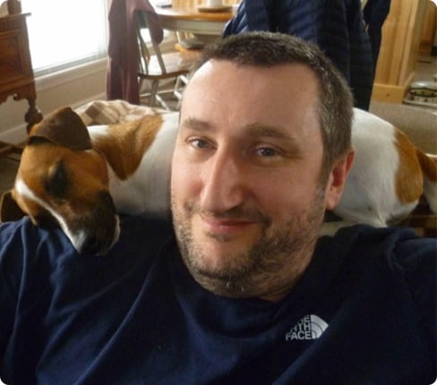 Picture of Simon, Executive Vice President, Global Data Operations at Parexel, he has his dog laying on his shoulders, while he is looking at the camera with a smile on his lips, he has short hair and wears a dark t-shirt..