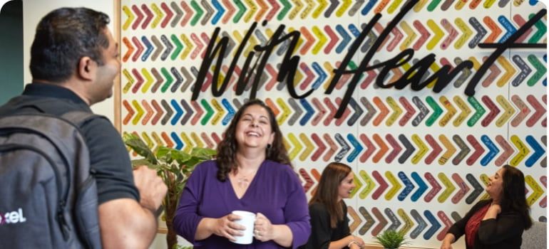 People seating in break room with a mural of the word "With Heart" on the wall.