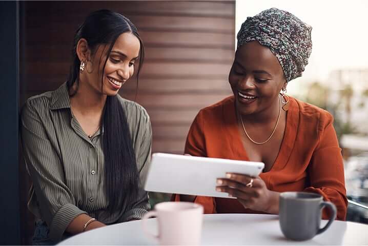 two women looking at a tablet over coffee and smiling