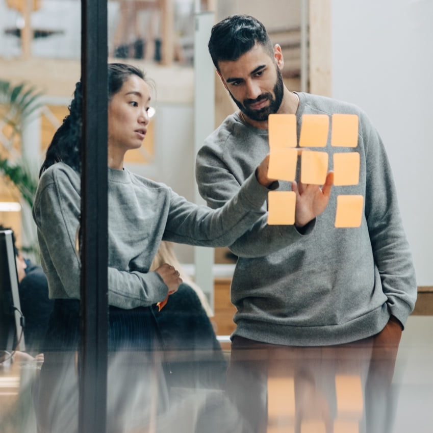 male and female employee looking at sticky notes on an office wall