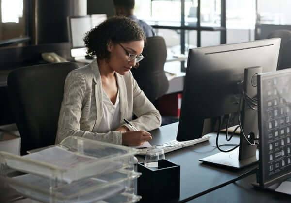 black female employee taking notes at her desk in front of a computer