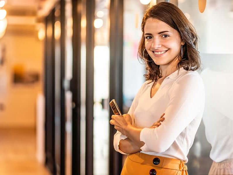 young female employee leaning against an office wall and smiling