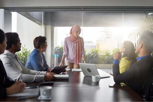 female employee wearing a hijab and addressing employees seated at a conference table